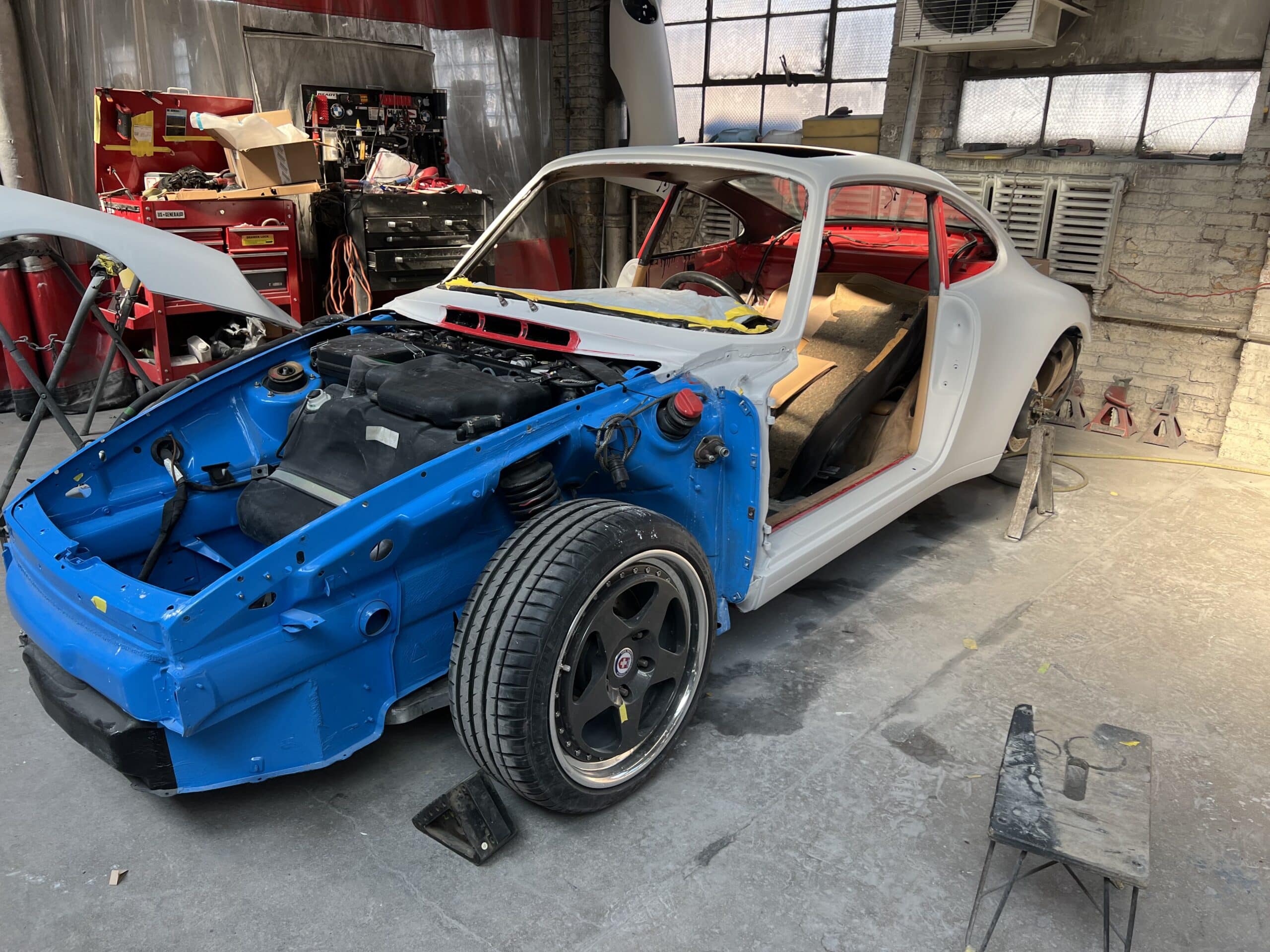 A mechanic is working on a car inside a well-equipped garage, surrounded by tools and equipment.