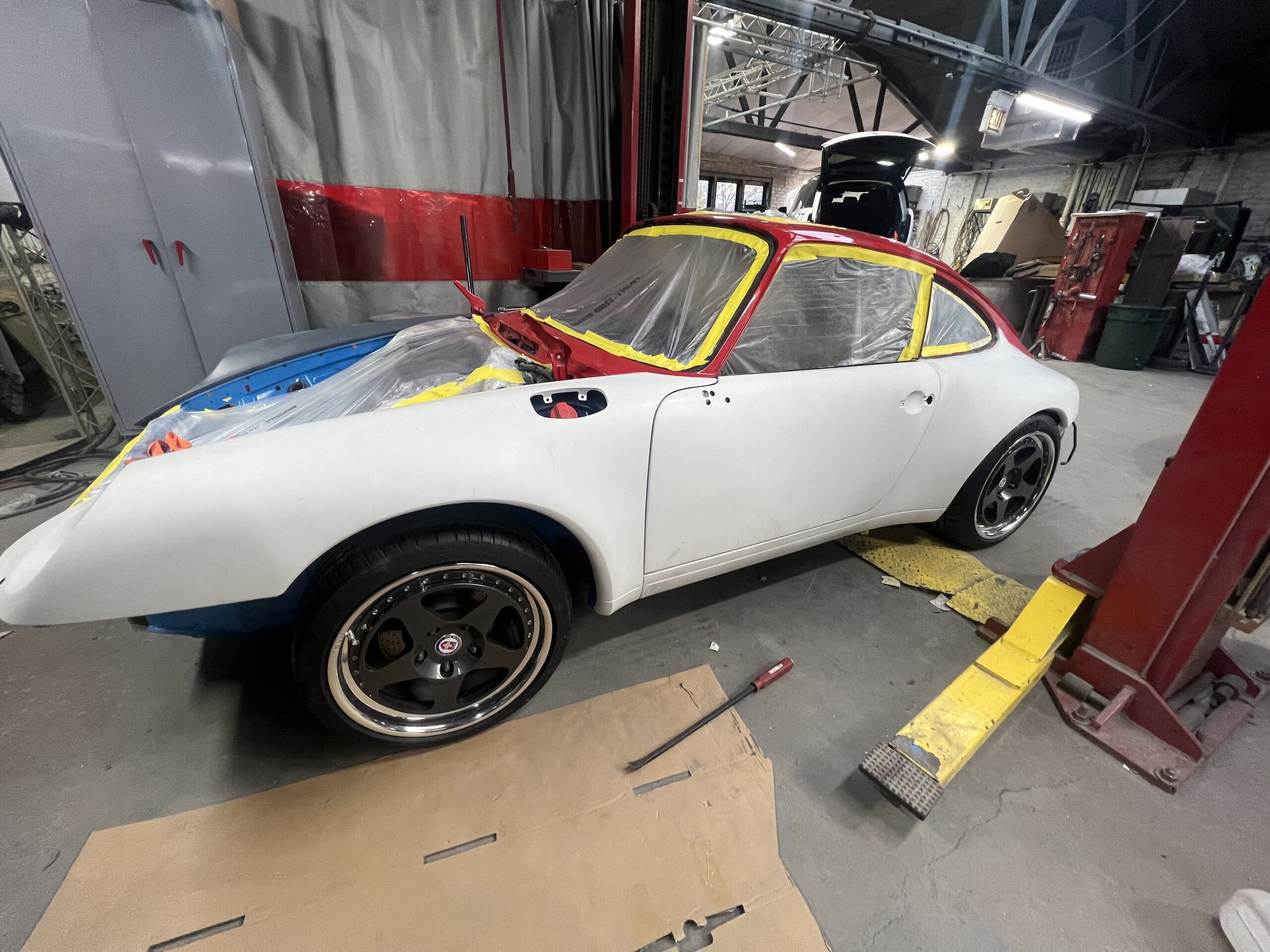 A car is lifted on a hydraulic jack in a garage, with a mechanic inspecting the engine and tools nearby.