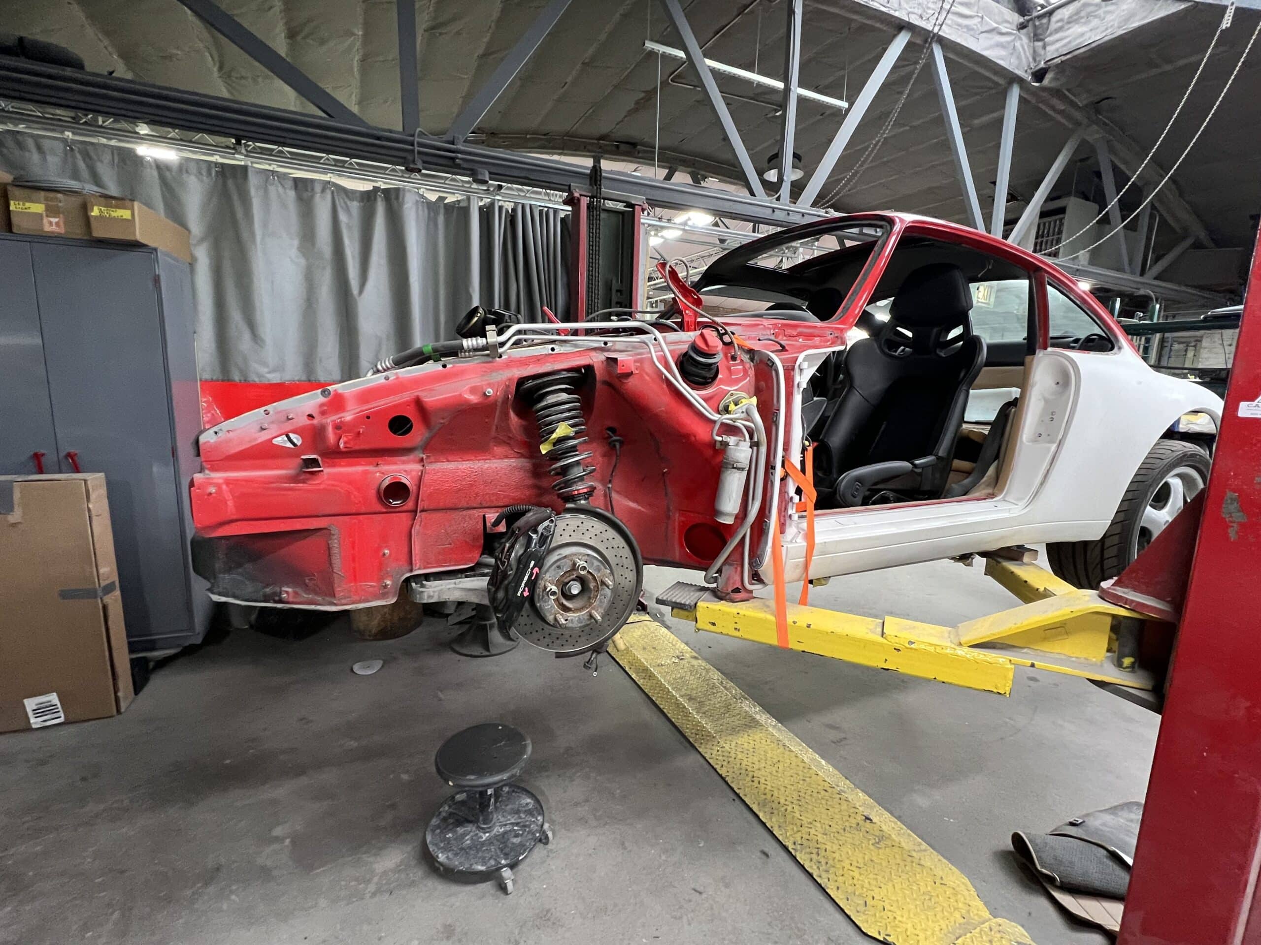 A red car is being repaired in a garage, with tools and equipment visible around it.