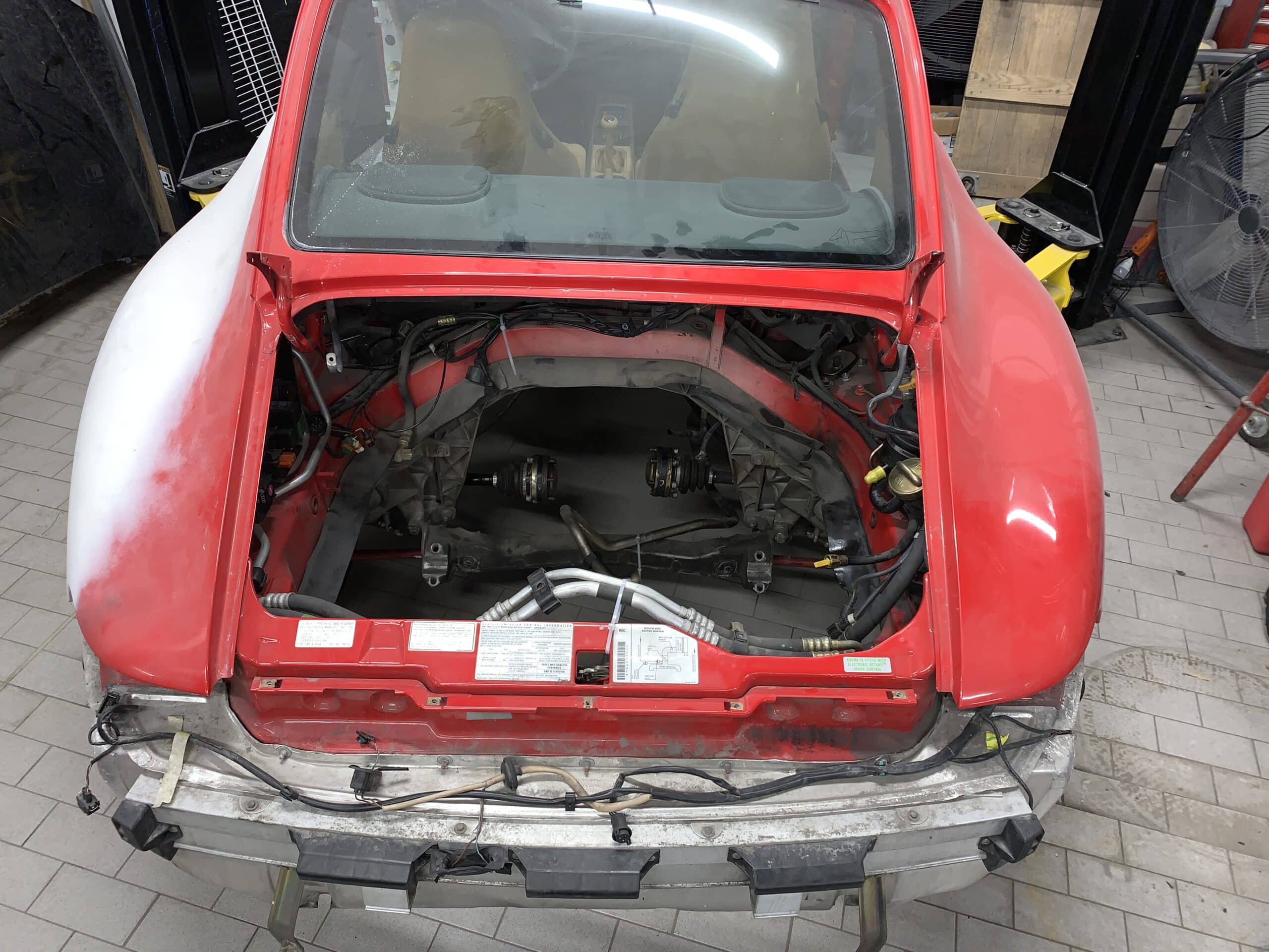 A mechanic works on a red car inside a garage, surrounded by various tools and parts.