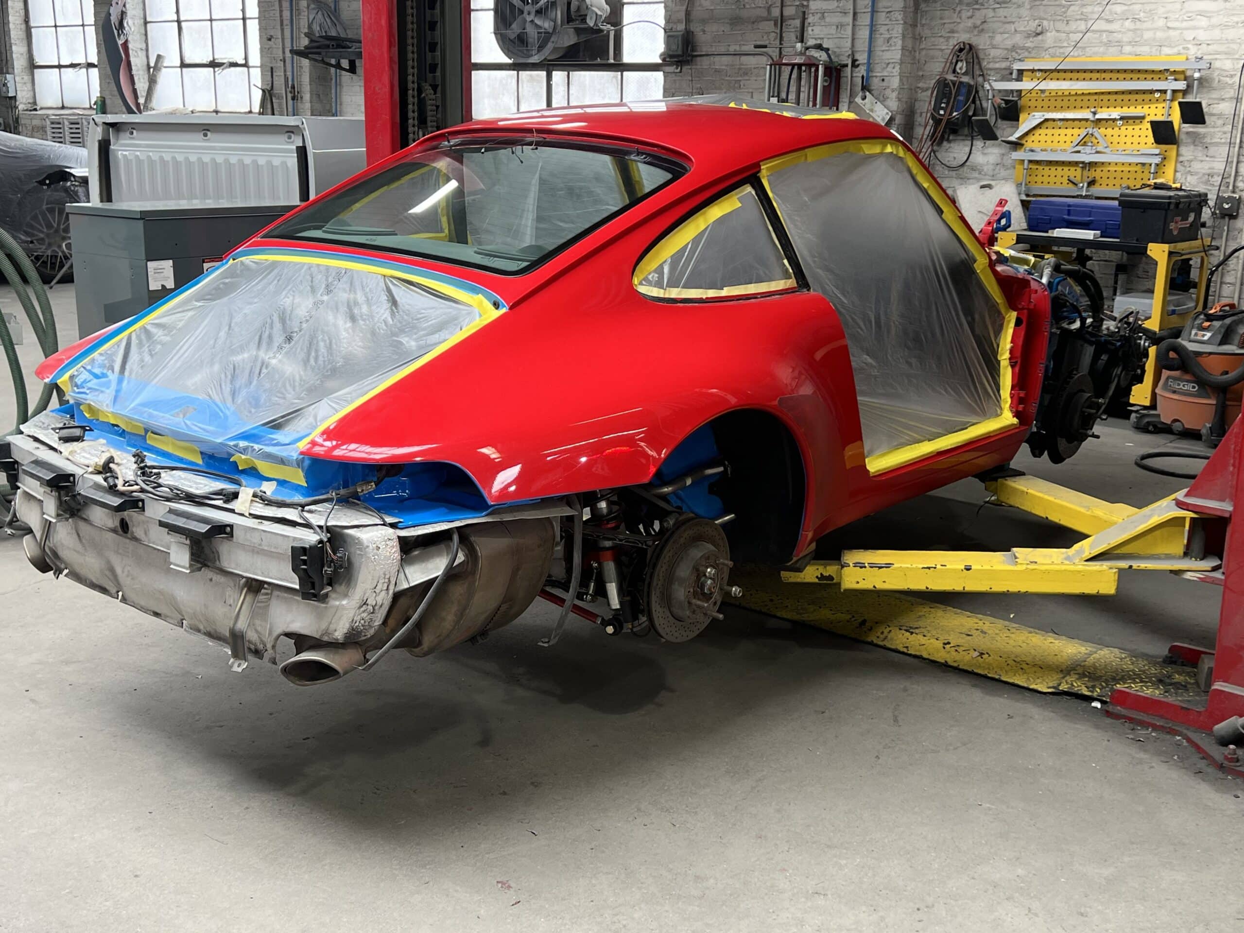 A mechanic works on a red car inside a garage, surrounded by various tools and parts.
