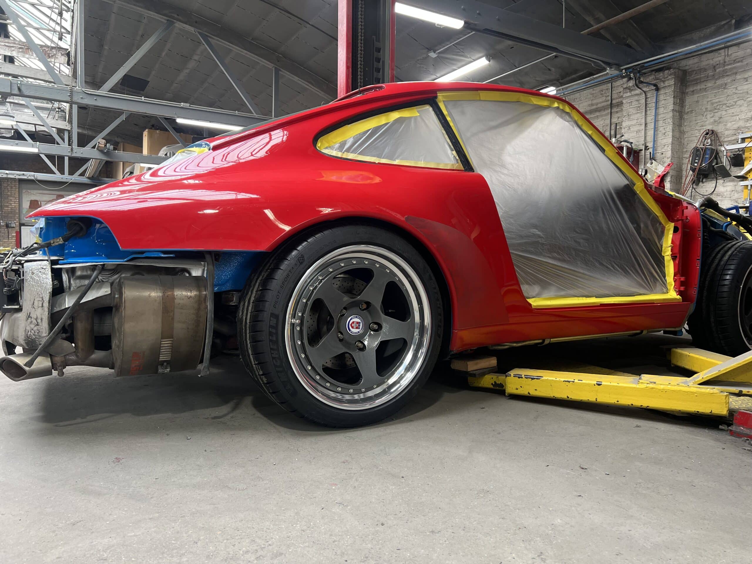 red car is under maintenance in a garage, with tools scattered on the workbench nearby.