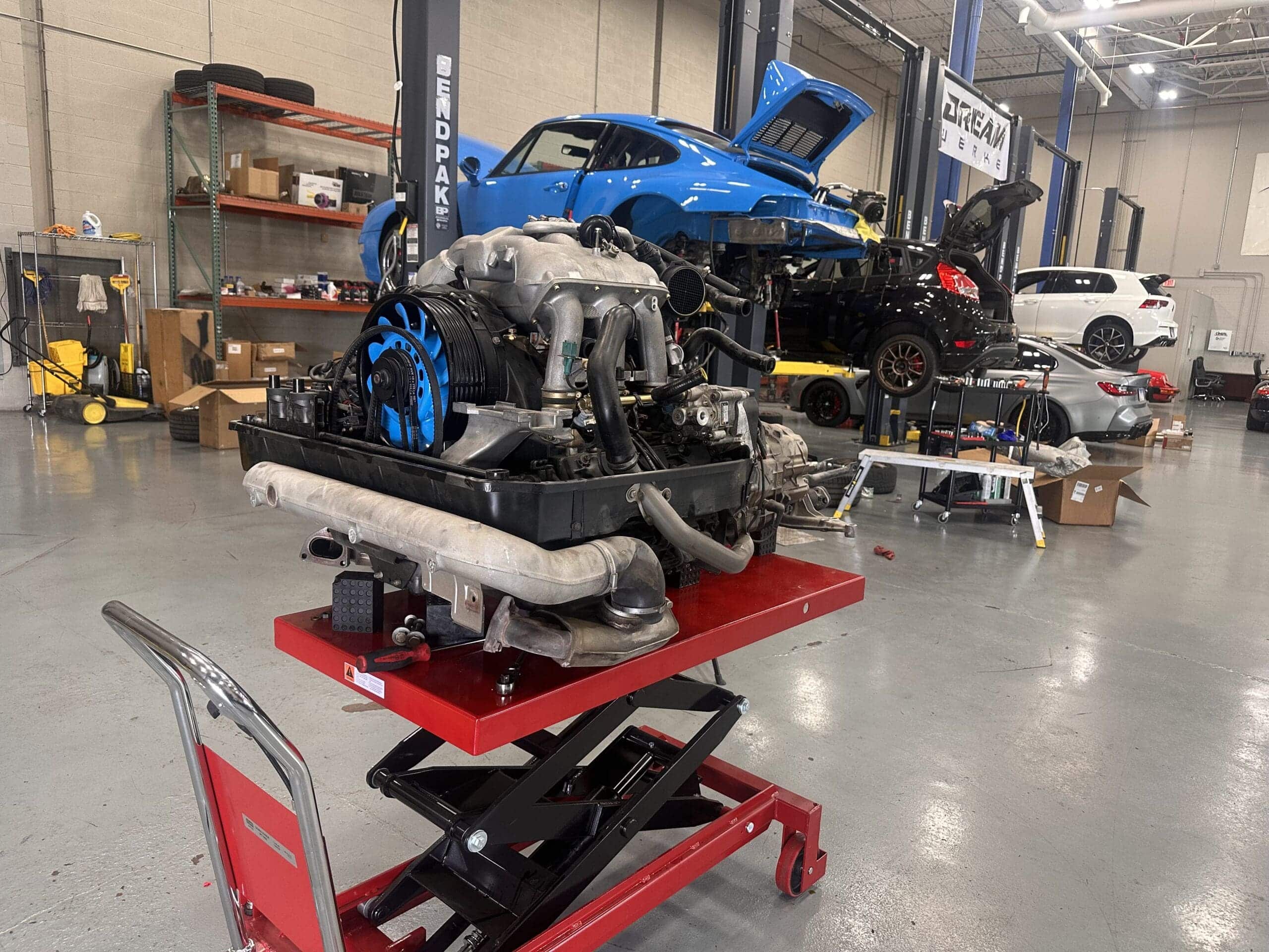 A car engine mounted on a work stand, positioned in a well-lit garage environment.