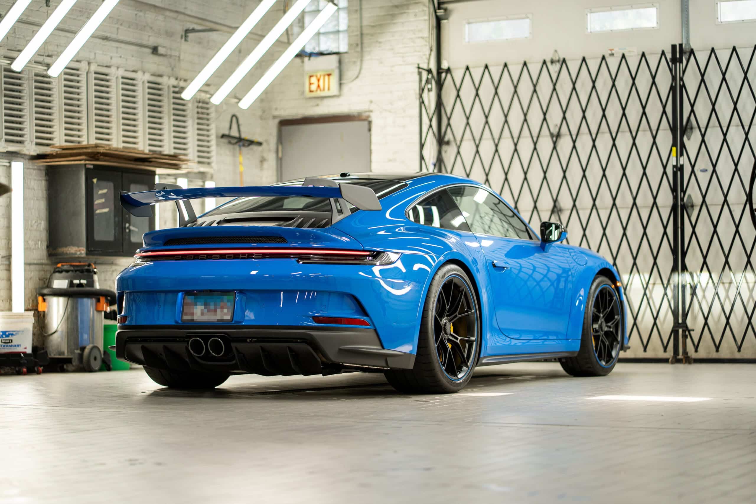 Rear view of a bright blue Porsche sitting in a mechanic's shop with light streaking across the paint