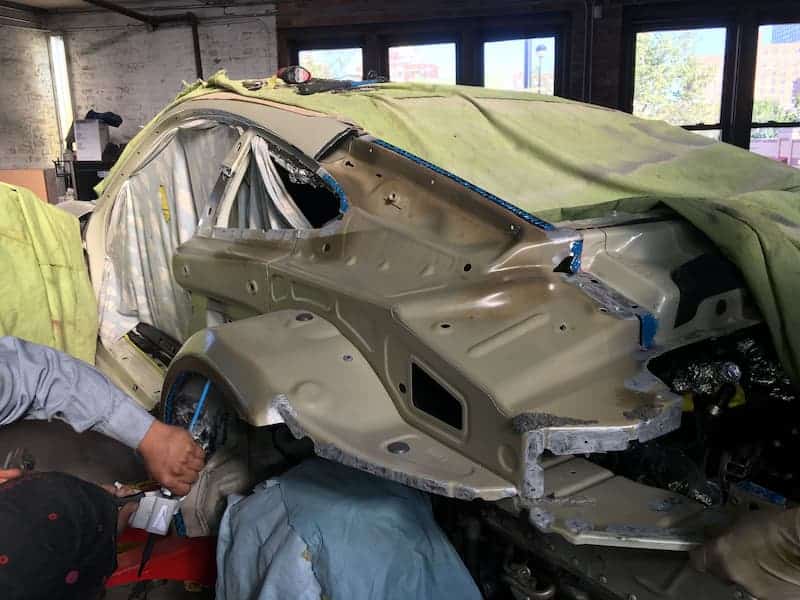 A man repairs a damaged car, focused on fixing the vehicle's exterior and assessing the extent of the damage.